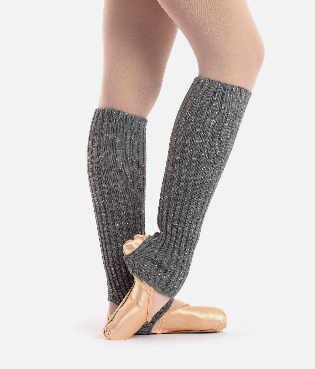 A close-up of a dancer's legs wearing dark gray ribbed leg warmers over light pink ballet slippers, set against a plain light gray background.