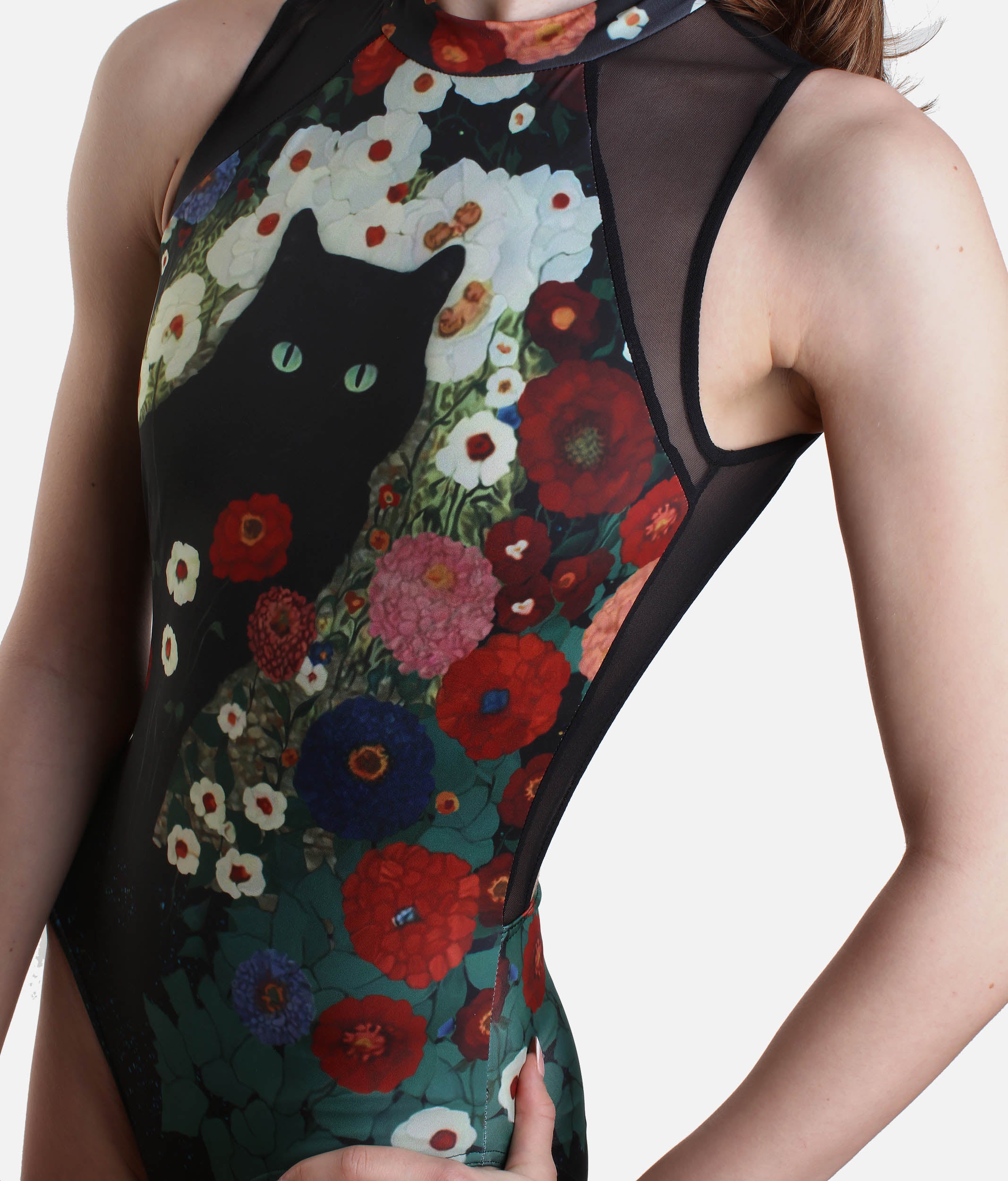 A close-up of a sleeveless bodysuit worn by a model, featuring a black cat and colorful wildflowers on a dark background with sheer mesh side panels.