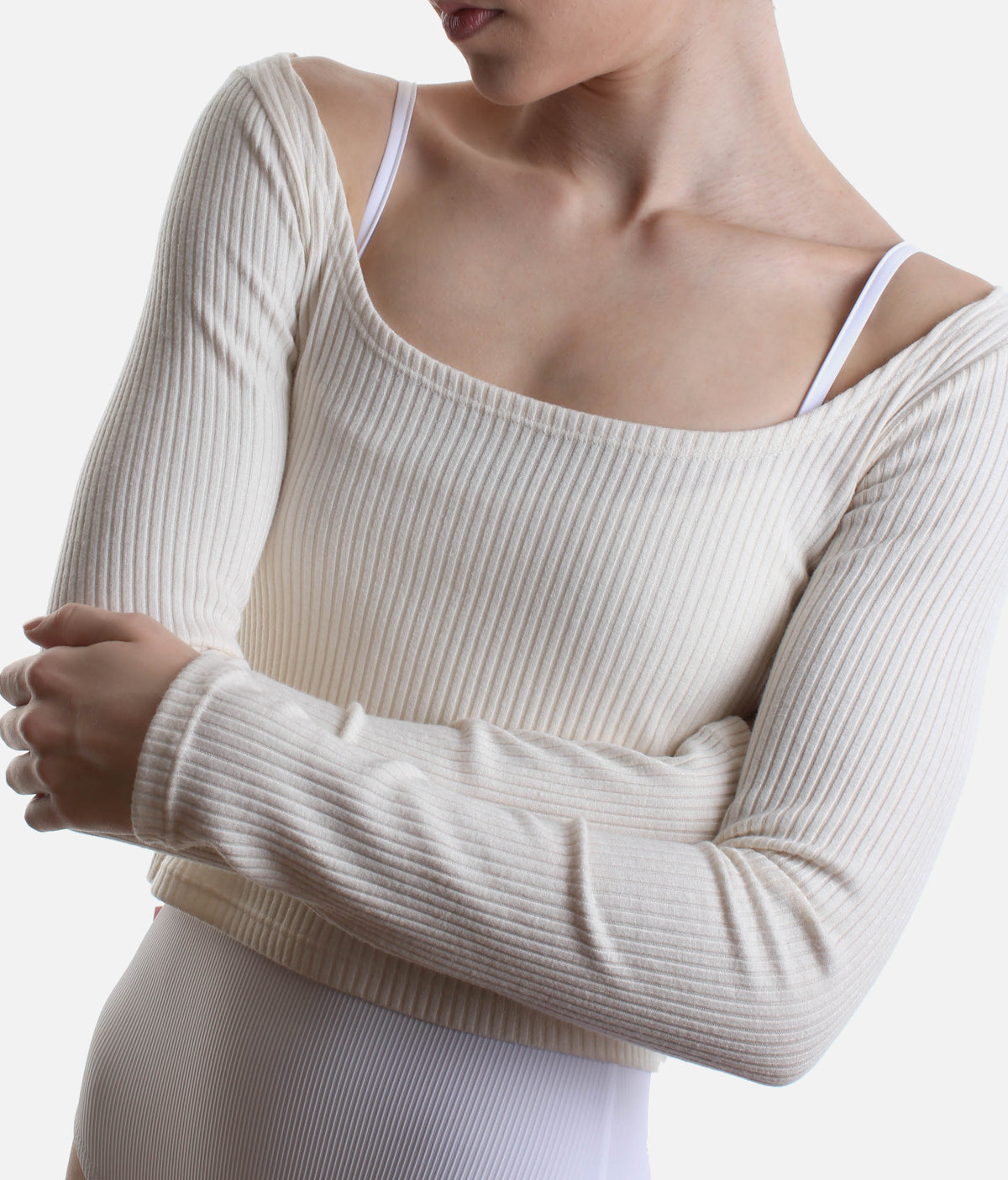 A close-up of a model wearing a ribbed long-sleeve scoop-neck top in cream, paired with matching ribbed bottoms against a plain light background.