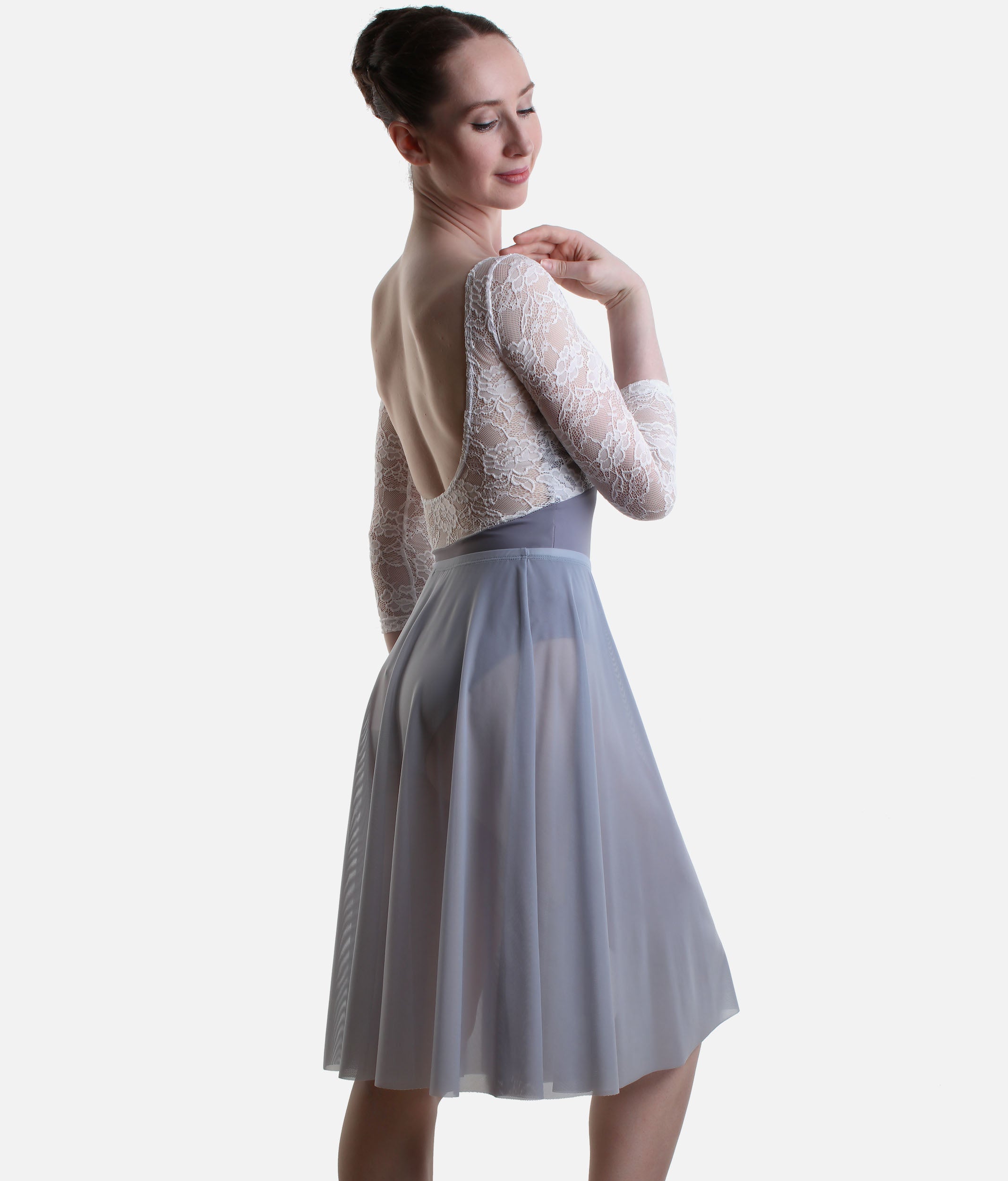 A woman modeling a three-piece dance leotard set featuring a light gray pleated skirt, a matching gray waistband, and a white lace long-sleeve top, shown from a three-quarter back angle against a light gray studio background.