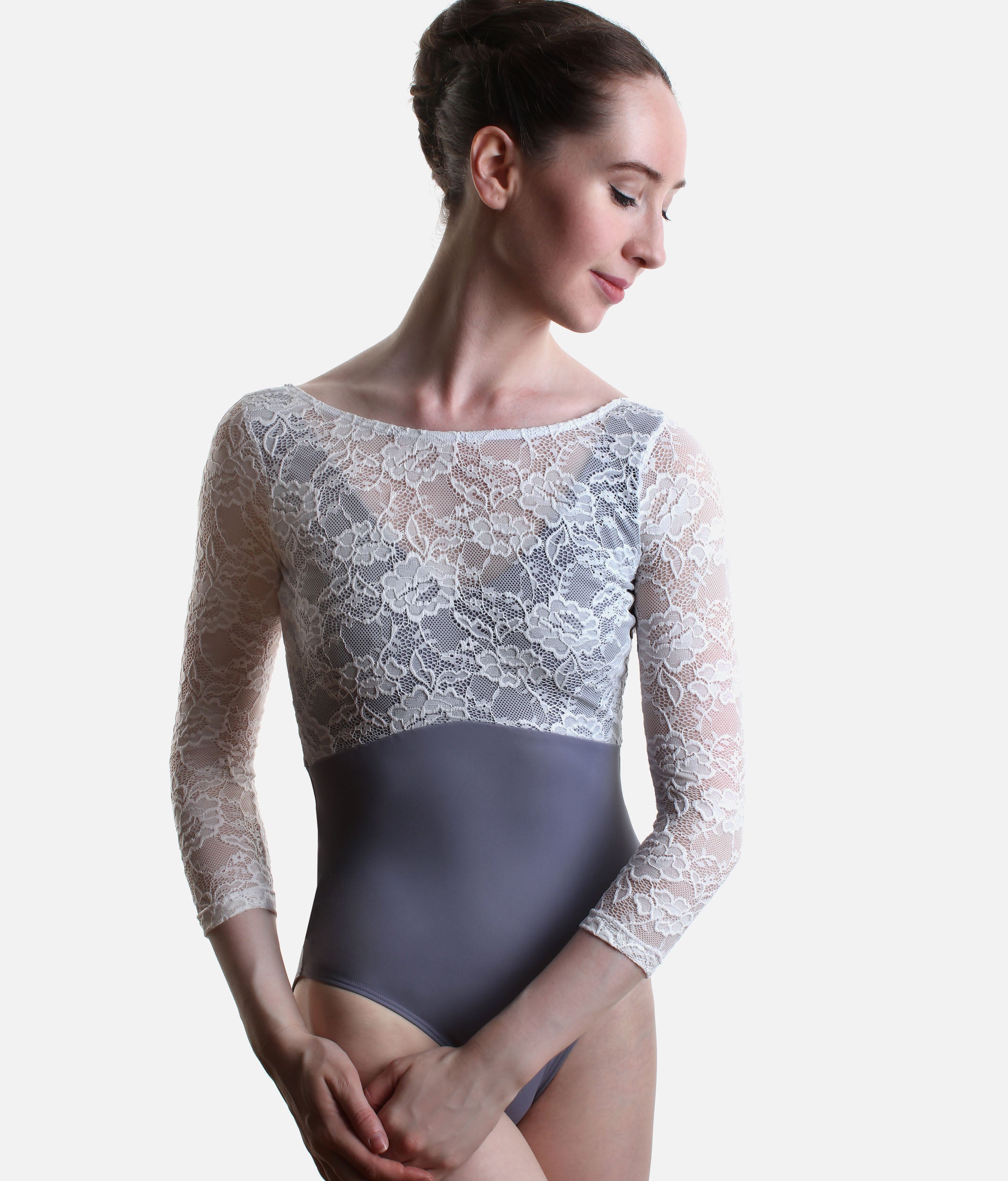 A female dancer wearing a three-quarter sleeve leotard with a white floral lace bodice and sleeves, and a solid dark gray waist and hip panel, posed against a light gray studio background.