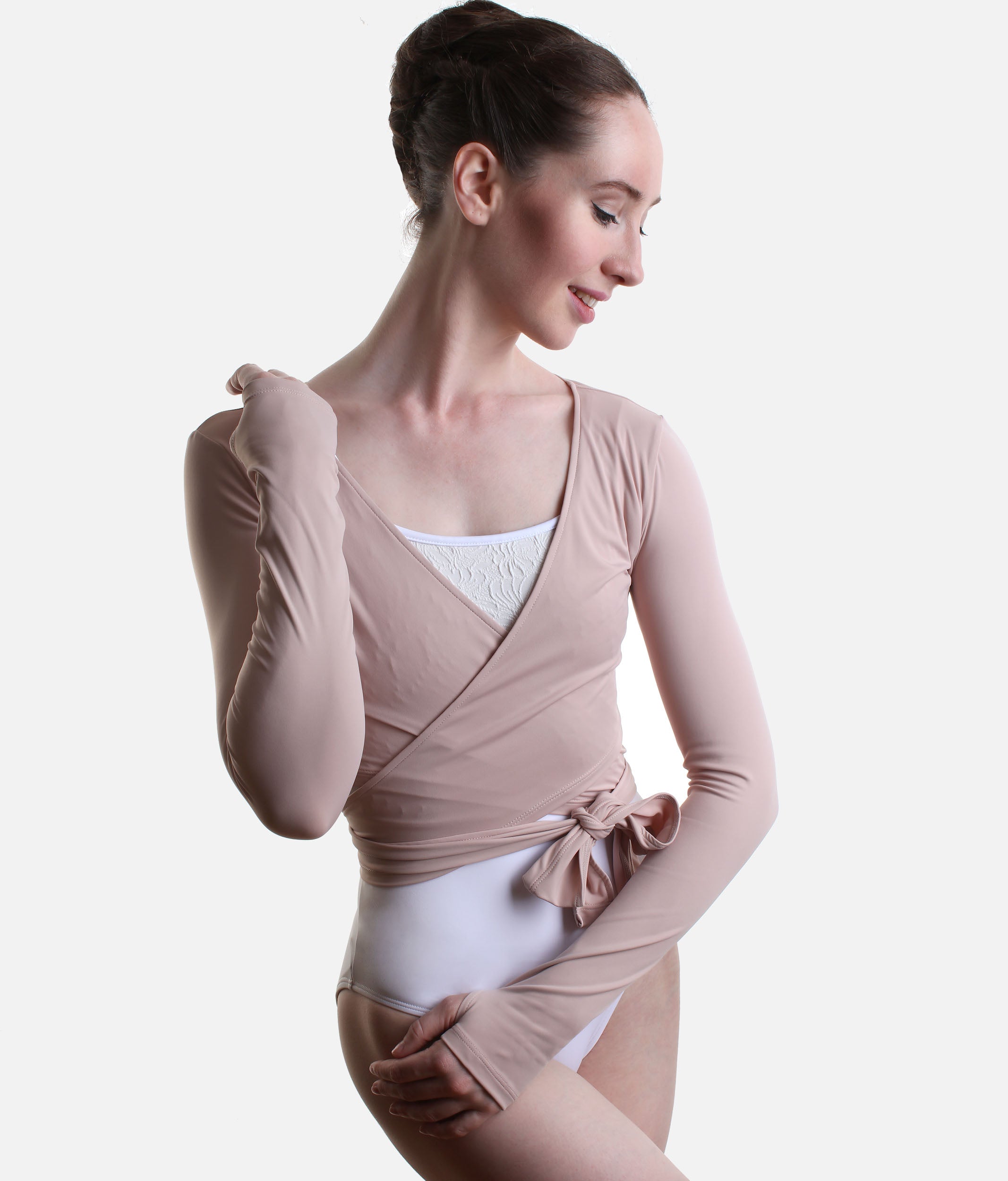 A woman modeling a long-sleeve, wrap-style dance leotard in a dusty rose color, worn over a white leotard, against a plain light gray background.